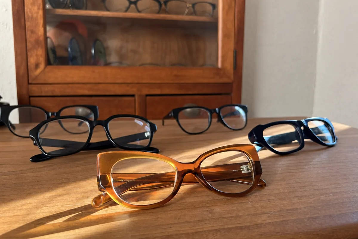 Monturas sin marca sobre un mostrador de madera, con una vitrina de óptica al fondo.