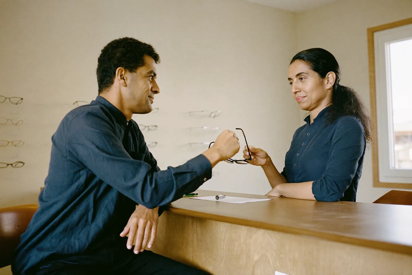 Optometrista peruana ayudando a un cliente a probarse una montura en una óptica con luz natural.